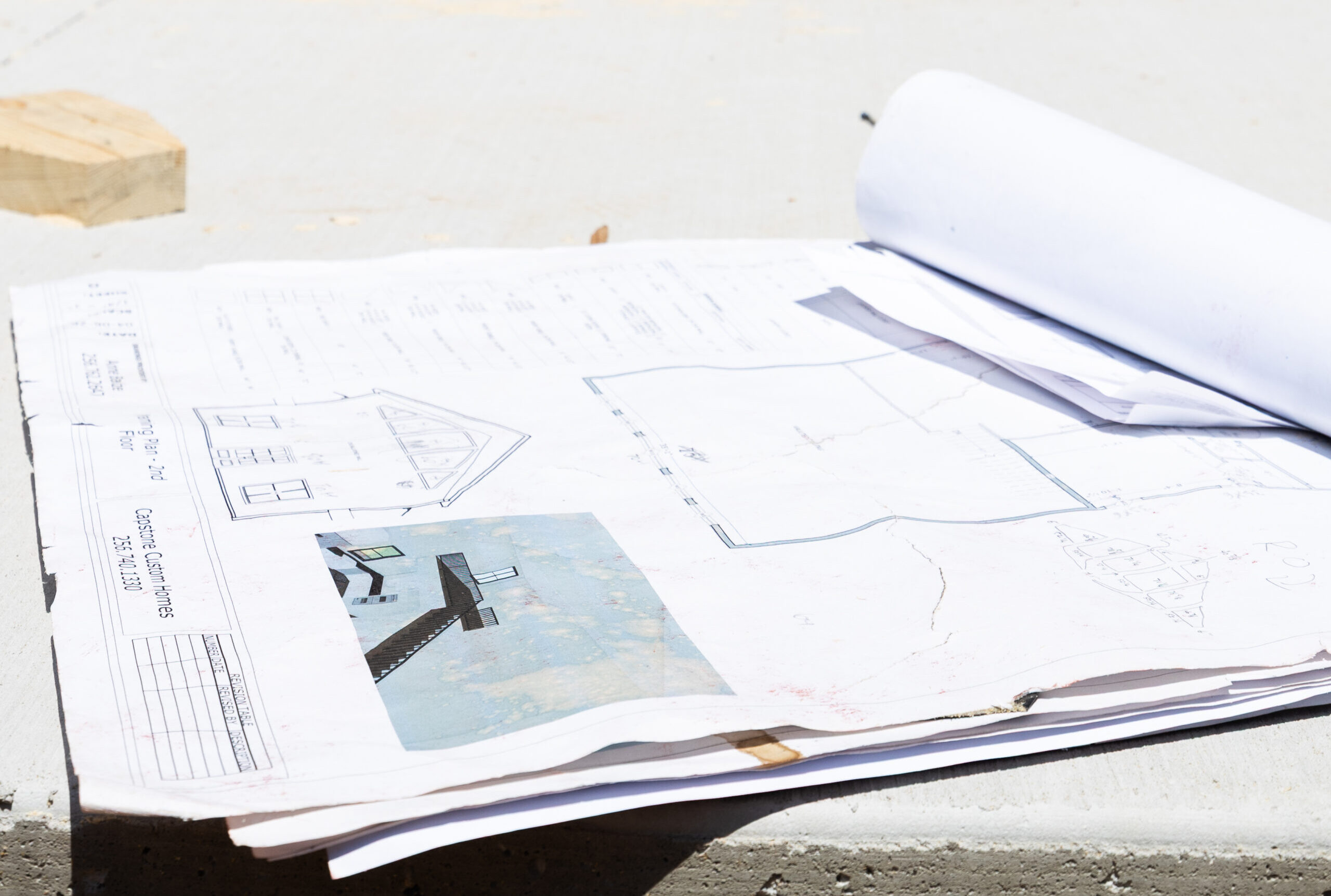Blueprint drawings spread on a wooden surface at a construction site, with architectural details visible on the pages.