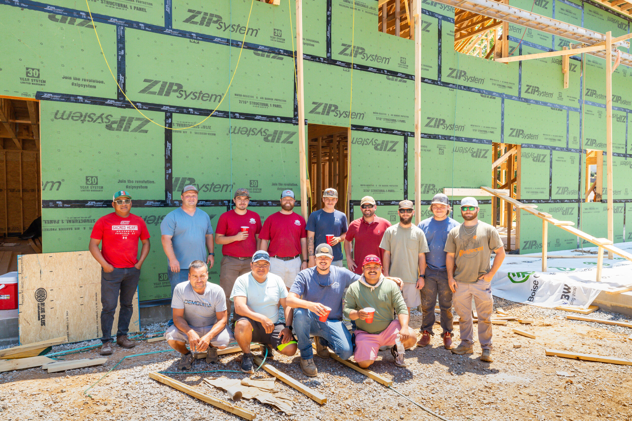 Group of construction workers posing in front of a partially framed house with green ZIP System sheathing and wooden framing.
