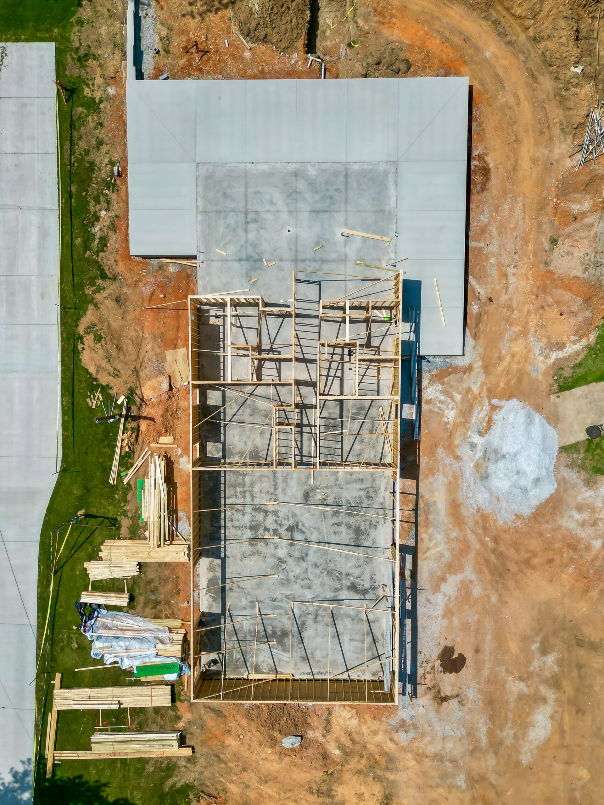 Aerial view of a building under construction with a wooden frame on a concrete foundation and scattered lumber surrounding it